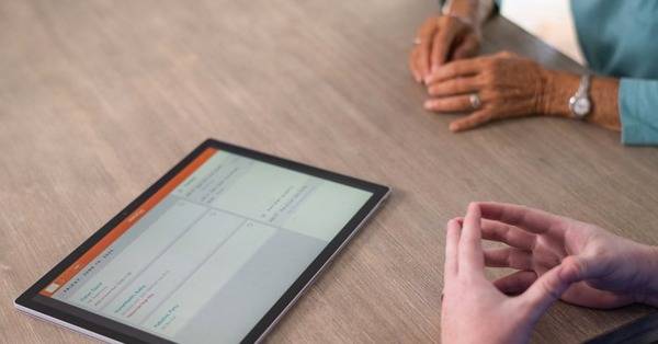 hands of healthcare professional and hands of elderly person on table with mobile tablet showing a dashboard