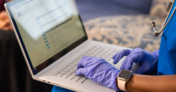 latex gloved hands of healthcare professional typing on laptop
