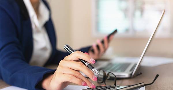 woman holding pen, looking at calculator