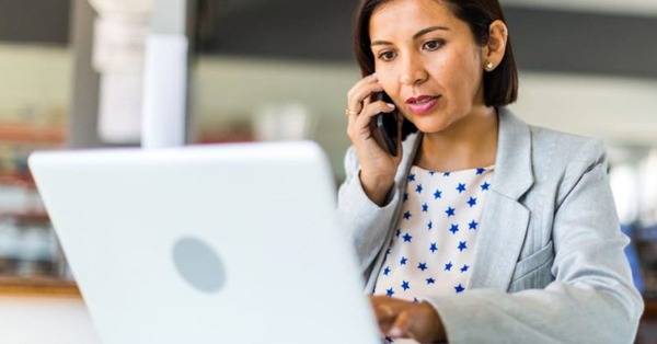 woman talks on smart phone while working on laptop