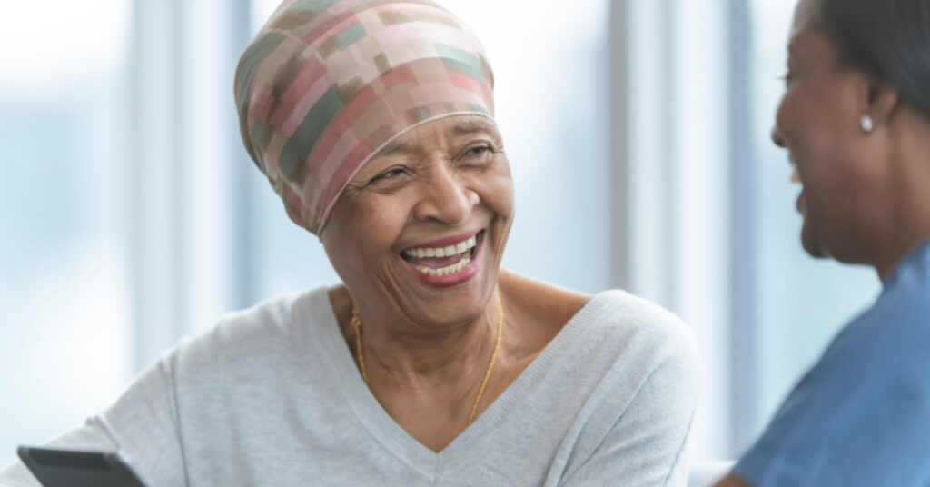 elderly woman in headwrap laughs with healthcare professional