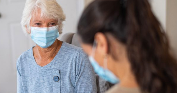 Elderly patient wearing a face mask talks person wearing a face mask
