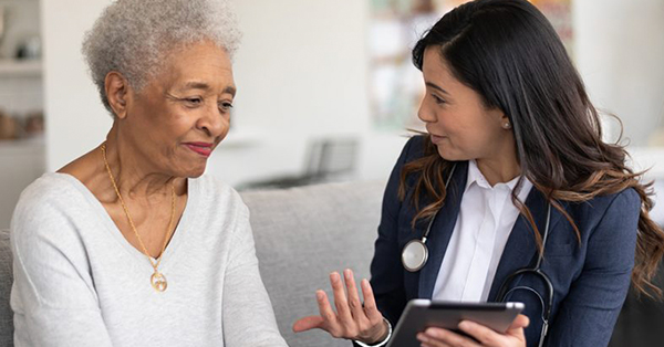 BIPOC healthcare provider speaks with elderly patient while using a mobile tablet