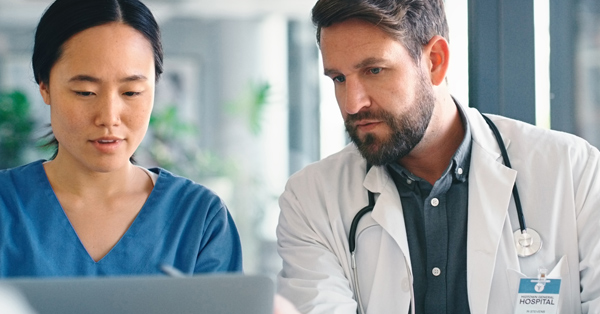 two healthcare professionals with hospital badges look at a laptop