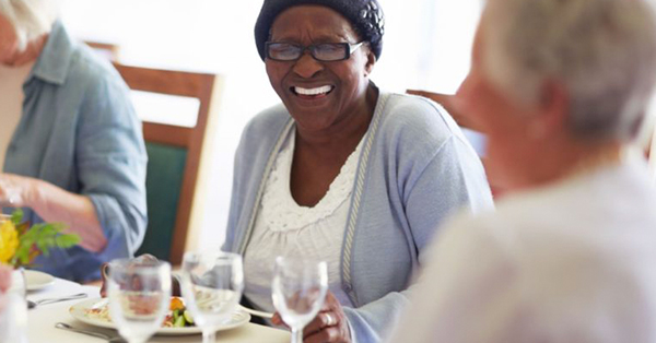 elderly person laughs while enjoying a meal with others