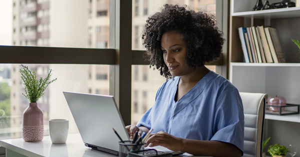 Black female doctor writing notes on a laptop