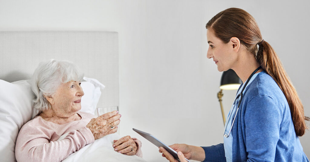 elderly woman drinks water in bed while talking to healthcare professional