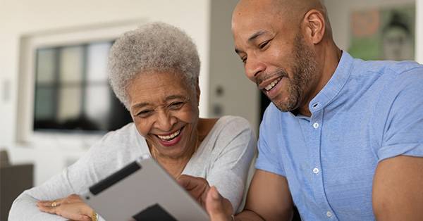 BIPOC male talks to elderly BIPOC woman while they look at digital tablet