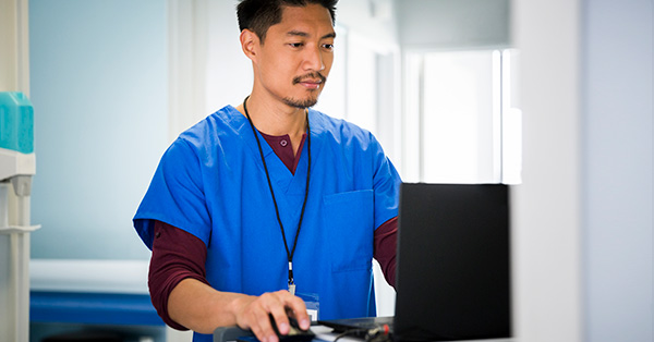healthcare professional works on laptop at workstation